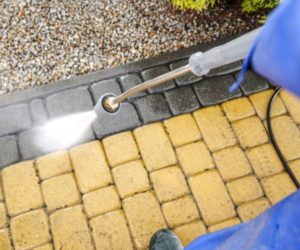 person washing white and grey external pavers with professional cleaning equipment